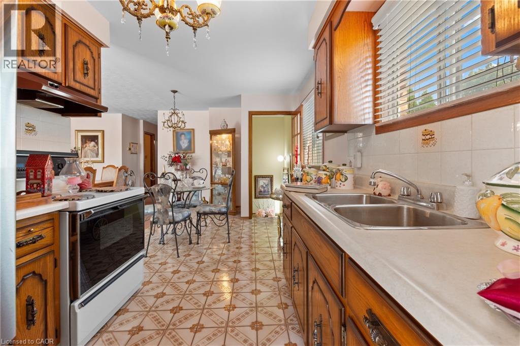 Kitchen featuring traditional wood cabinetry, a double basin stainless steel sink, and white tile backsplash. - 202 Ray Street N, Hamilton, ON - Indoor Photo Showing Kitchen With Double Sink