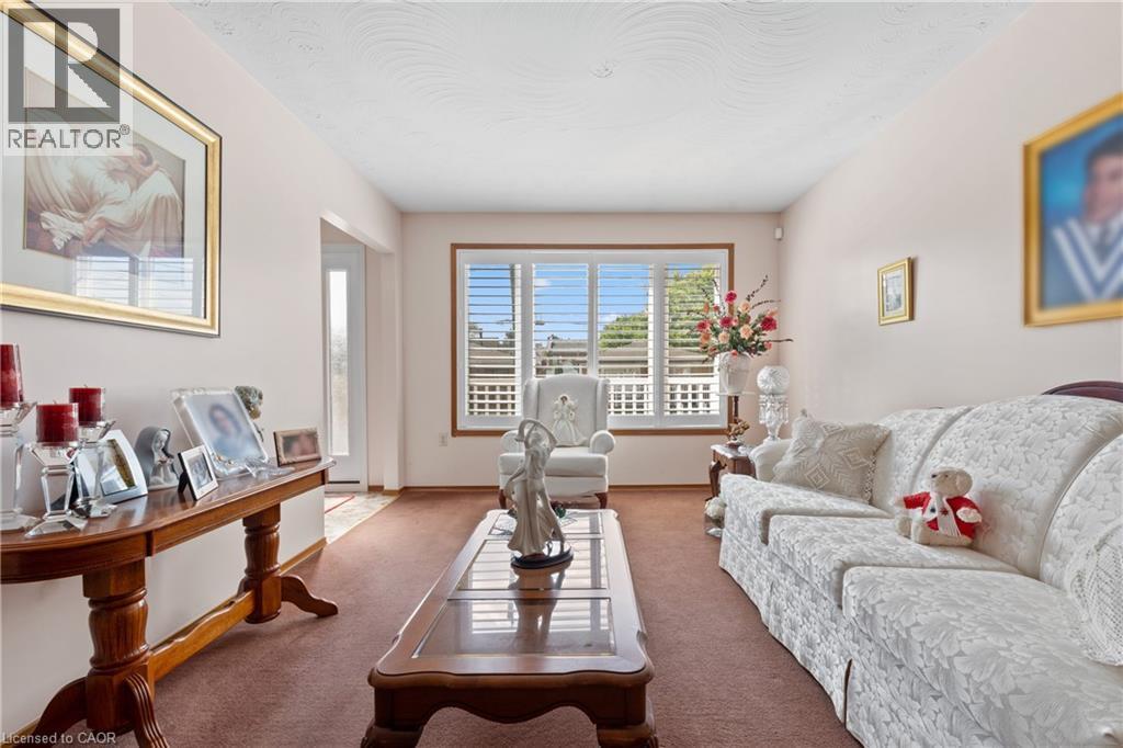 Living area featuring plush carpeting, a large window with white louvered shutters, and a textured ceiling. - 202 Ray Street N, Hamilton, ON - Indoor Photo Showing Living Room