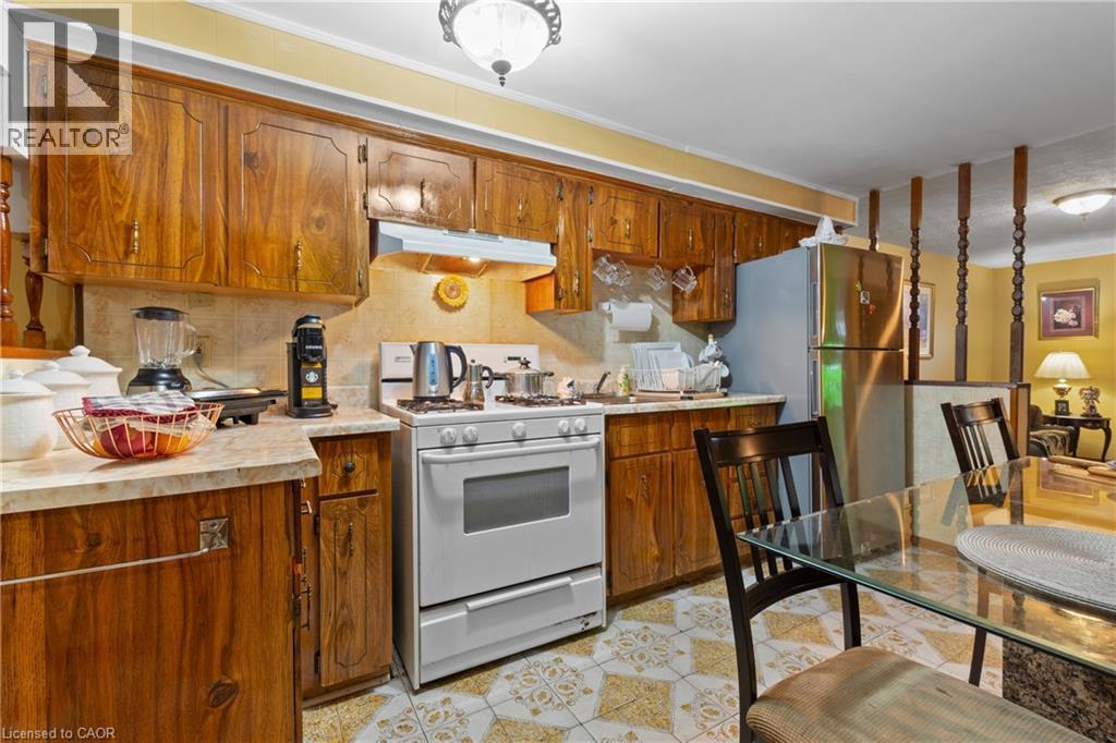 Kitchen featuring extensive wood cabinetry, stone-finish countertops, tile backsplash, and patterned tile flooring. - 202 Ray Street N, Hamilton, ON - Indoor Photo Showing Kitchen