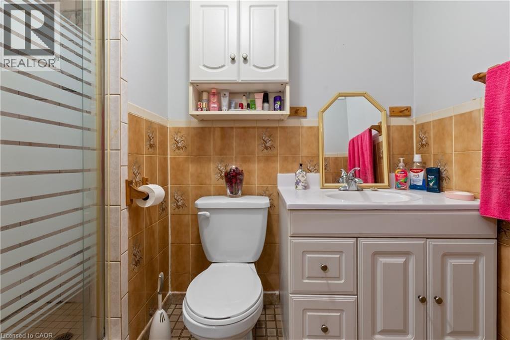Bathroom featuring a glass-enclosed shower, a white vanity with an integrated sink, a wall-mounted mirror, a toilet, and an overhead storage cabinet. - 202 Ray Street N, Hamilton, ON - Indoor Photo Showing Bathroom