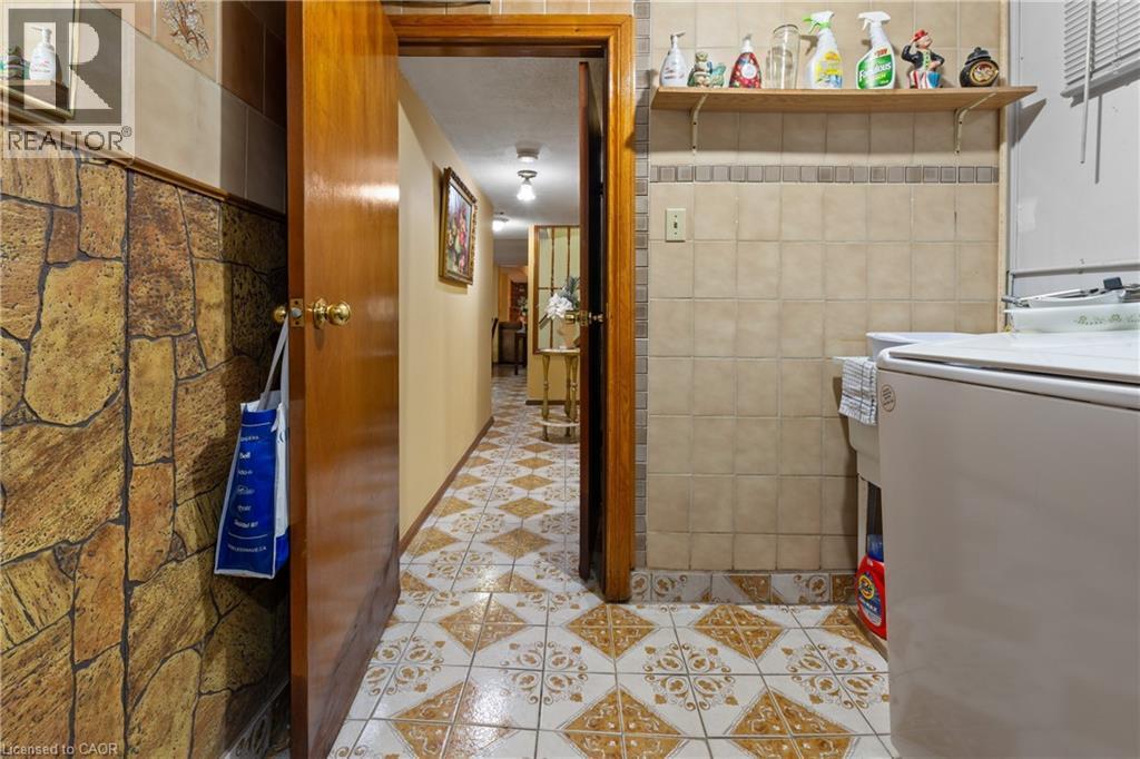Hallway featuring patterned tile flooring, a solid wood door, and a stone-look accent wall. - 202 Ray Street N, Hamilton, ON - Indoor Photo Showing Laundry Room