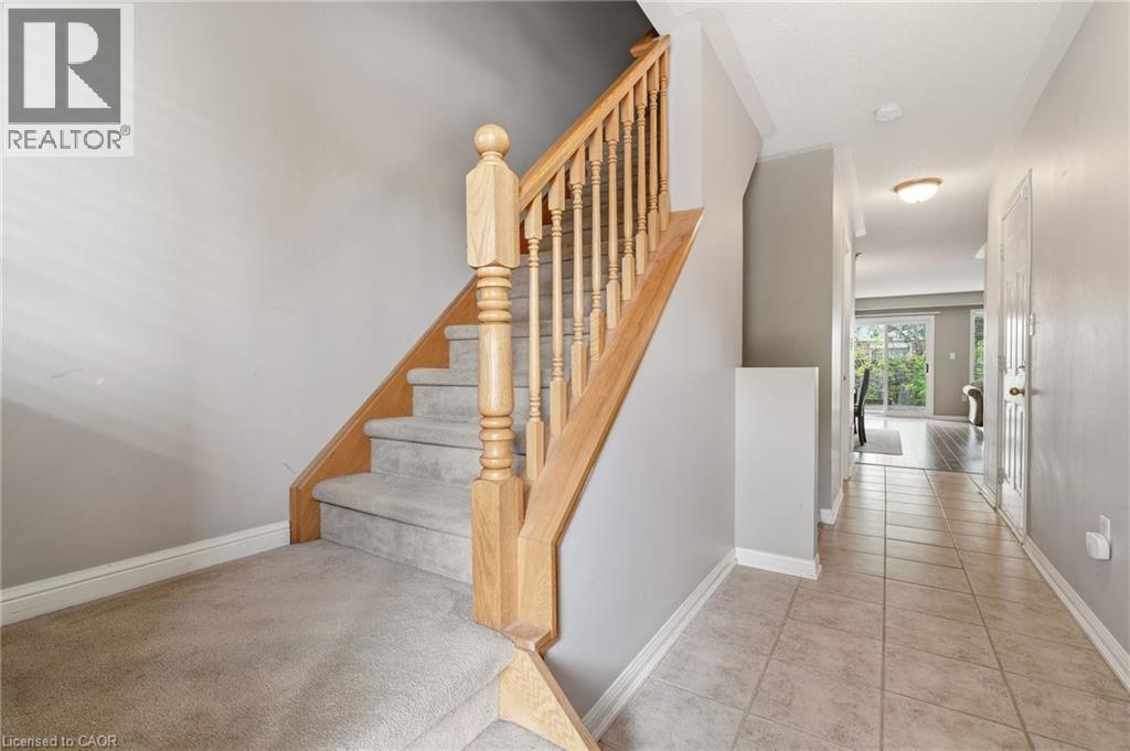 Foyer featuring light-toned tile flooring, a carpeted staircase with wood handrail, and a white paneled interior door - 4413 Peter Drive, Burlington, ON