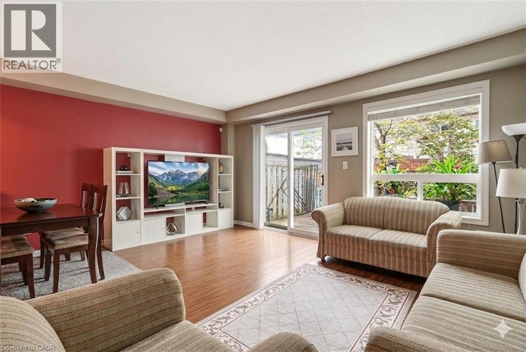 Open-concept living area featuring wood-finish flooring, a contemporary built-in media console, a dining area with a dark wood table, and a sliding glass door leading to an outdoor space - 4413 Peter Drive, Burlington, ON