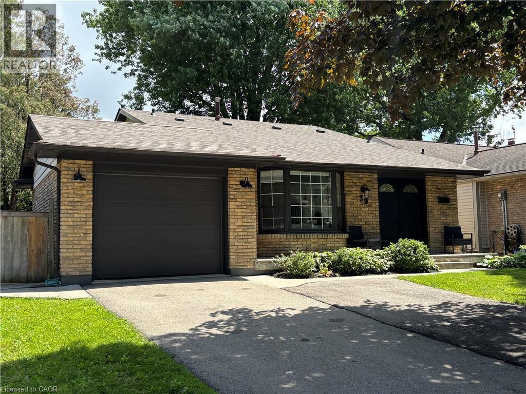 Brick facade residence featuring a dark garage door, paved driveway, mature landscaping, and a covered entry with dual dark doors - 39 Forestgate Drive, Hamilton, ON