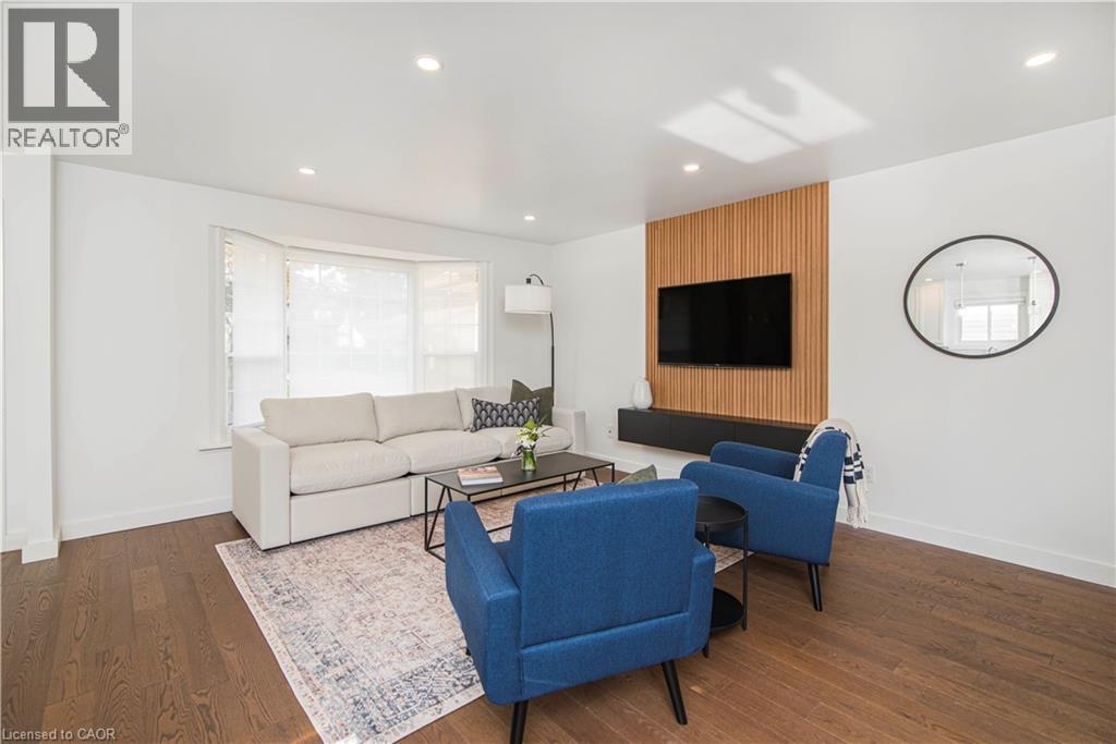 Living area featuring wood-finish flooring, a bay window with window treatments, a recessed lighting scheme, a wood-slat accent wall, and a wall-mounted media console - 39 Forestgate Drive, Hamilton, ON