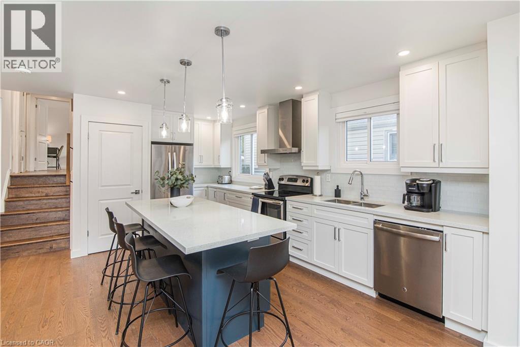 Modern kitchen featuring a large island with seating, white shaker-style cabinetry, stainless steel appliances, and wood-finish flooring - 39 Forestgate Drive, Hamilton, ON