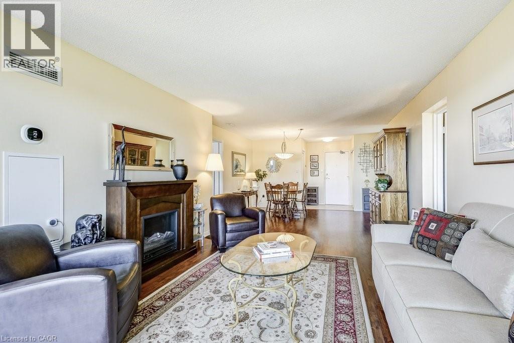 Living area featuring wood-finish flooring, a fireplace with a dark wood mantel, and light-colored walls - 1201 North Shore Boulevard E Unit# 706, Burlington, ON - Indoor Photo Showing Living Room With Fireplace