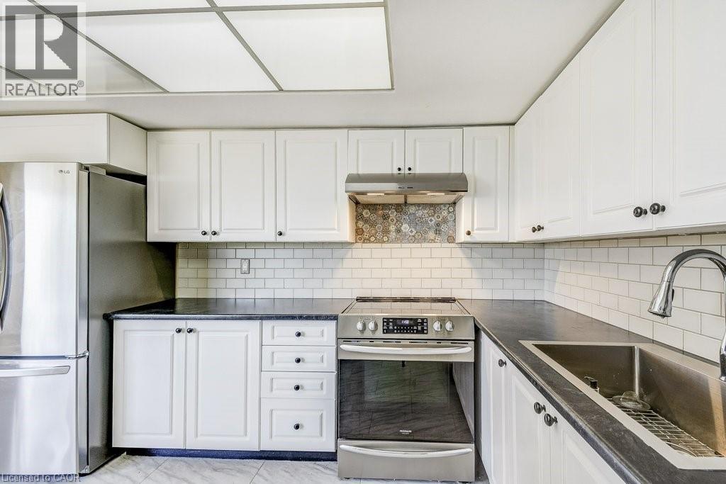 Kitchen featuring white cabinetry, dark countertops, a subway tile backsplash, stainless steel appliances, and tile flooring - 1201 North Shore Boulevard E Unit# 706, Burlington, ON - Indoor Photo Showing Kitchen