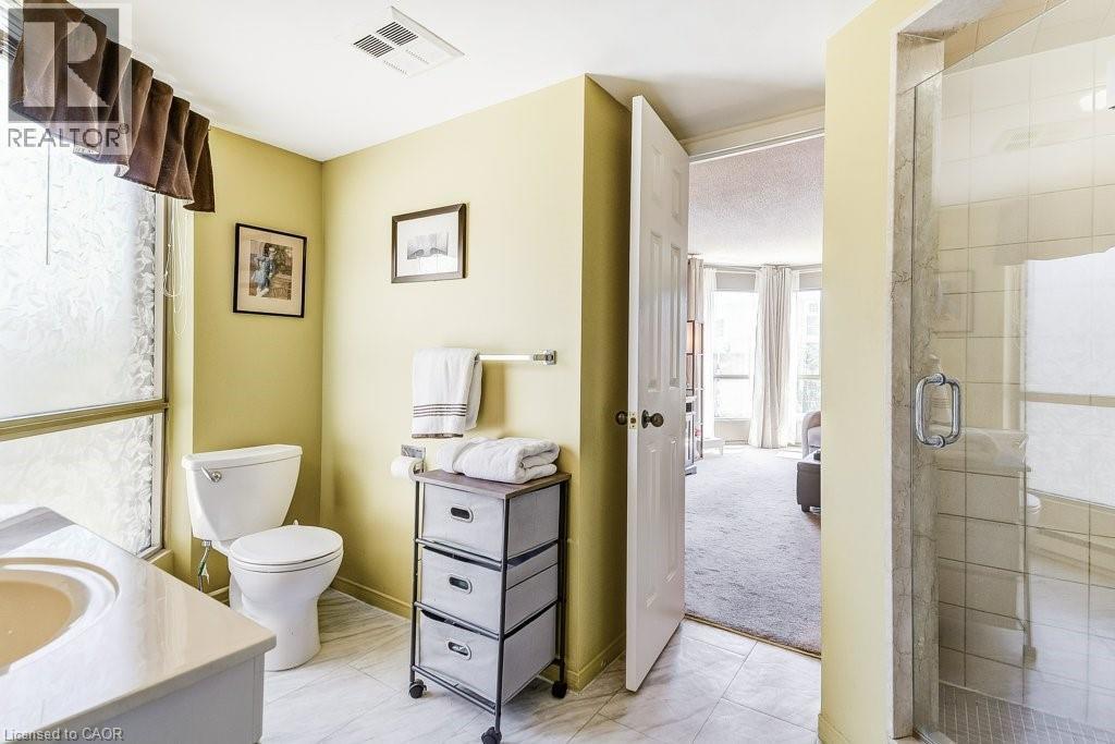 Bathroom featuring a vanity with an integrated sink, a toilet, and a tiled shower enclosure with a glass door - 1201 North Shore Boulevard E Unit# 706, Burlington, ON - Indoor Photo Showing Bathroom