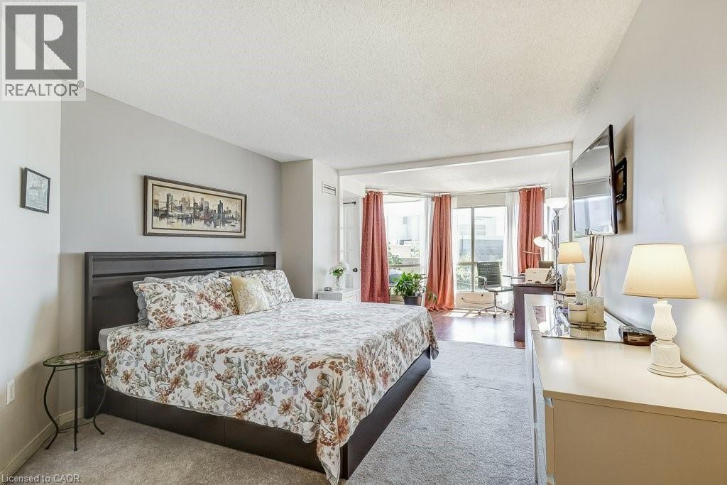Spacious sleeping area featuring light gray walls and plush carpeting, opening to a bright alcove - 1201 North Shore Boulevard E Unit# 706, Burlington, ON - Indoor Photo Showing Bedroom