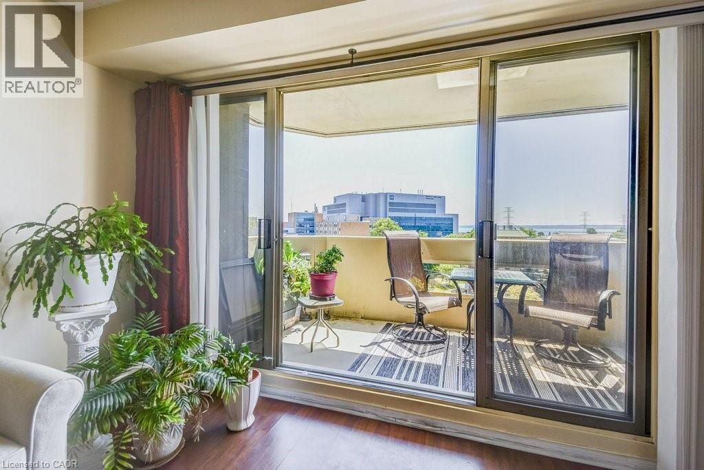 Sliding glass doors opening to a private balcony featuring a textured railing and an urban backdrop - 1201 North Shore Boulevard E Unit# 706, Burlington, ON - Indoor Photo Showing Other Room