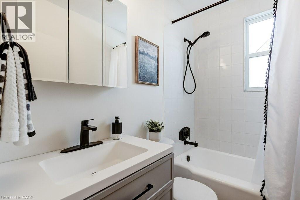 Bathroom featuring a white integrated sink with a matte black faucet, a medicine cabinet with mirrored doors, and a full-size bathtub with white subway tile surround and matte black fixtures - 202 Erindale Avenue, Hamilton, ON