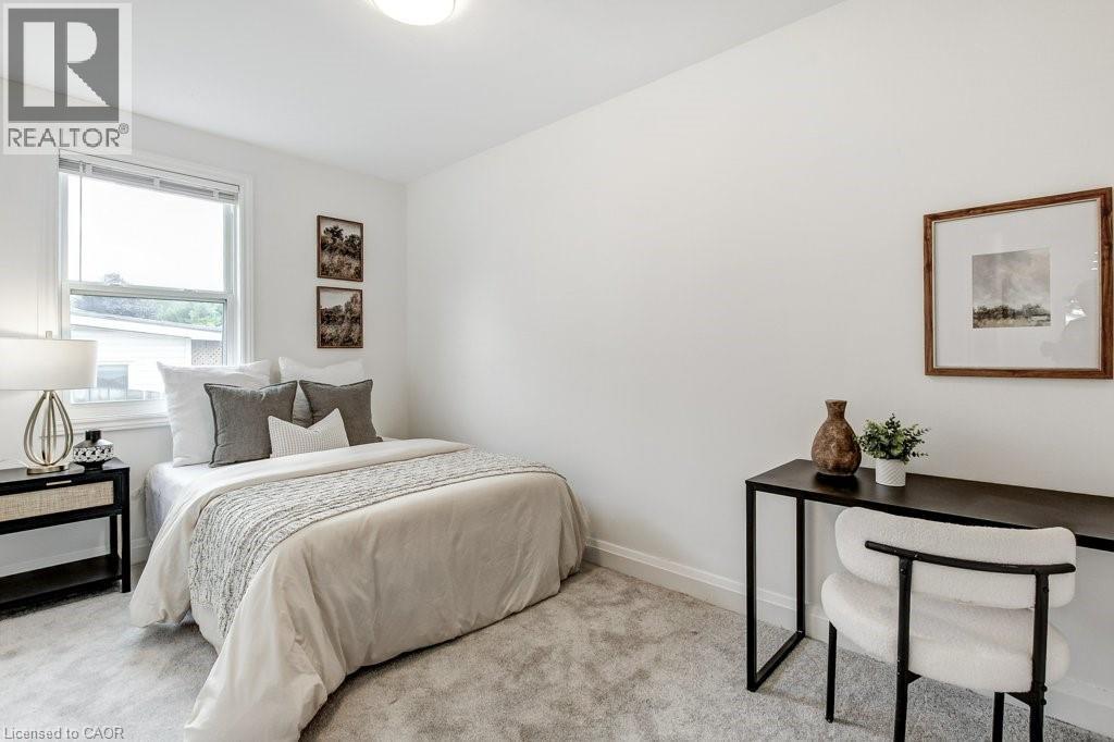 Bright interior space featuring a window with blinds, light-toned wall-to-wall carpeting, crisp white walls, white baseboards, and a flush-mount ceiling light fixture - 202 Erindale Avenue, Hamilton, ON