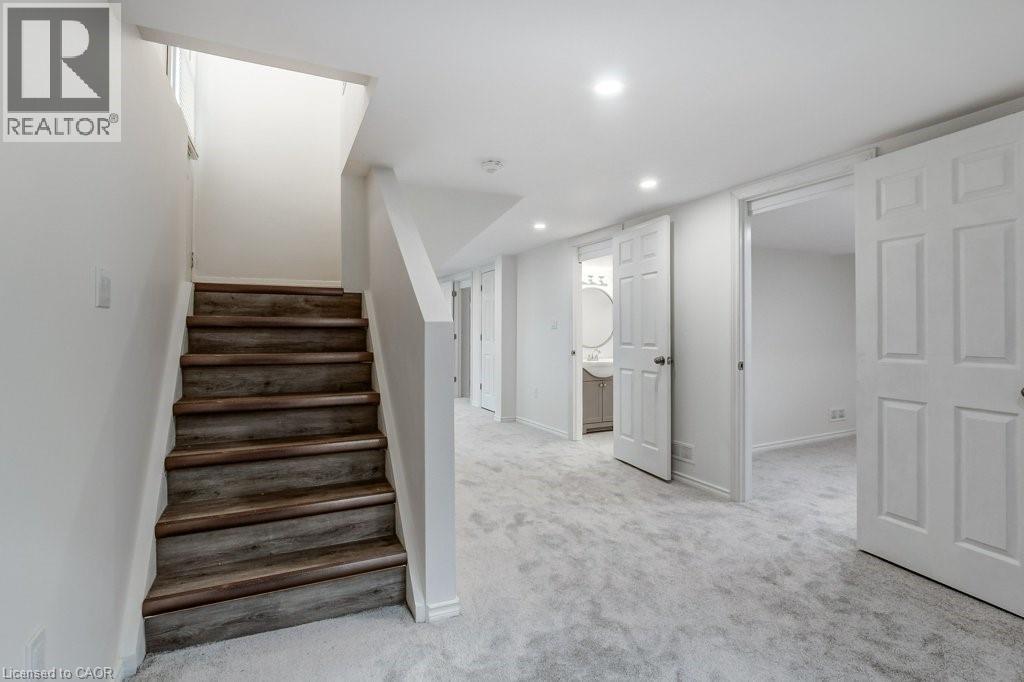 Finished lower level featuring wood-finish stairs, light gray carpeting, recessed lighting, white paneled doors, and a partial bathroom with a circular mirror and vanity - 202 Erindale Avenue, Hamilton, ON