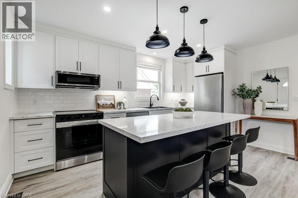 Modern kitchen featuring white shaker cabinetry, a large center island with seating, stainless steel appliances, a white subway tile backsplash, and light wood-finish flooring - 202 Erindale Avenue, Hamilton, ON