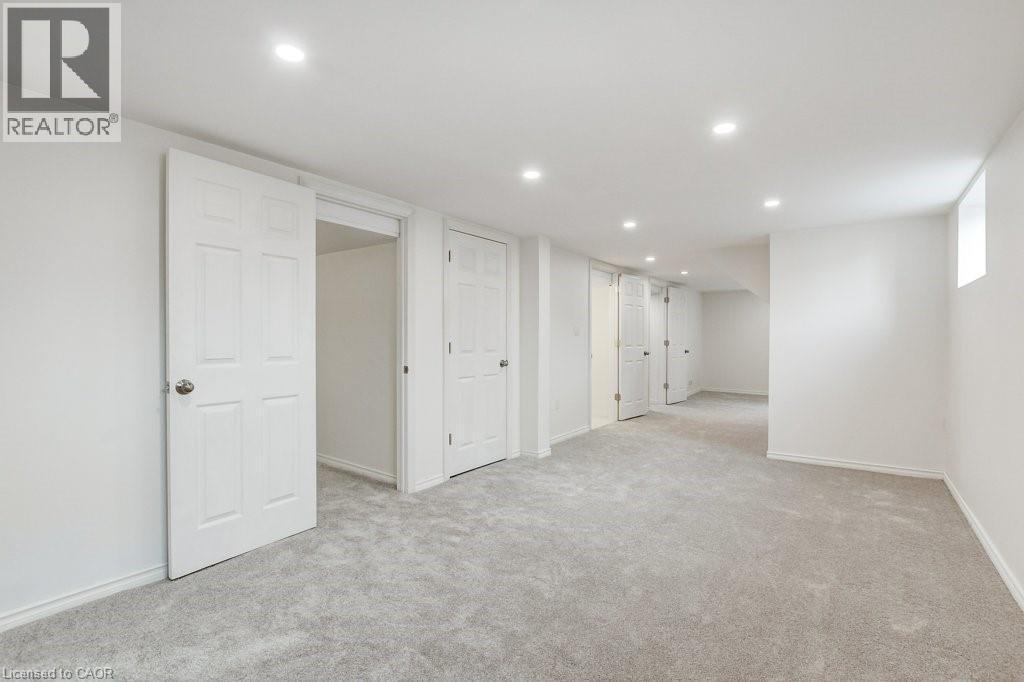Spacious lower-level room featuring light gray carpeting, recessed ceiling lighting, multiple paneled doors, and a high-set window - 202 Erindale Avenue, Hamilton, ON