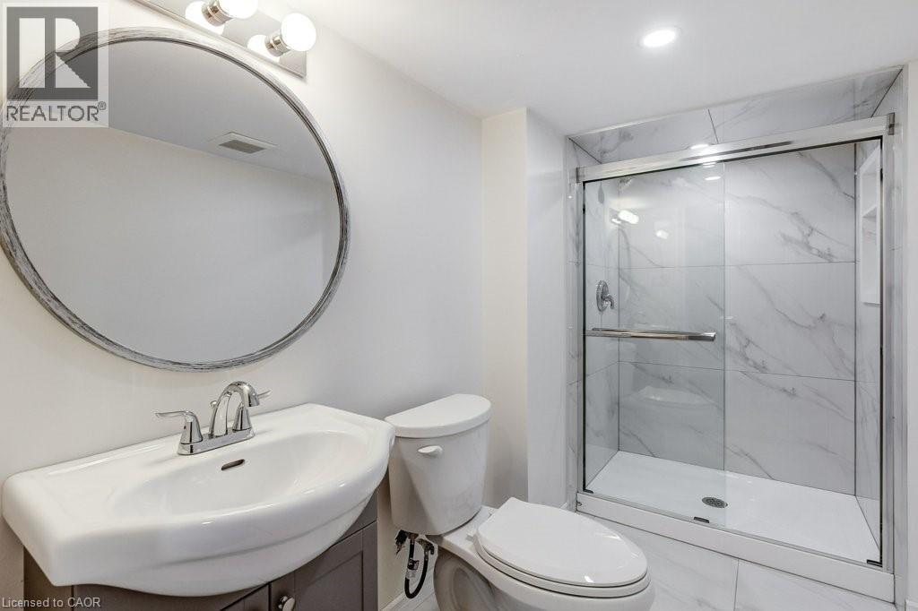 Bathroom featuring a glass-enclosed shower with large format marble-look tile, a modern vanity with integrated sink, and a circular mirror - 202 Erindale Avenue, Hamilton, ON