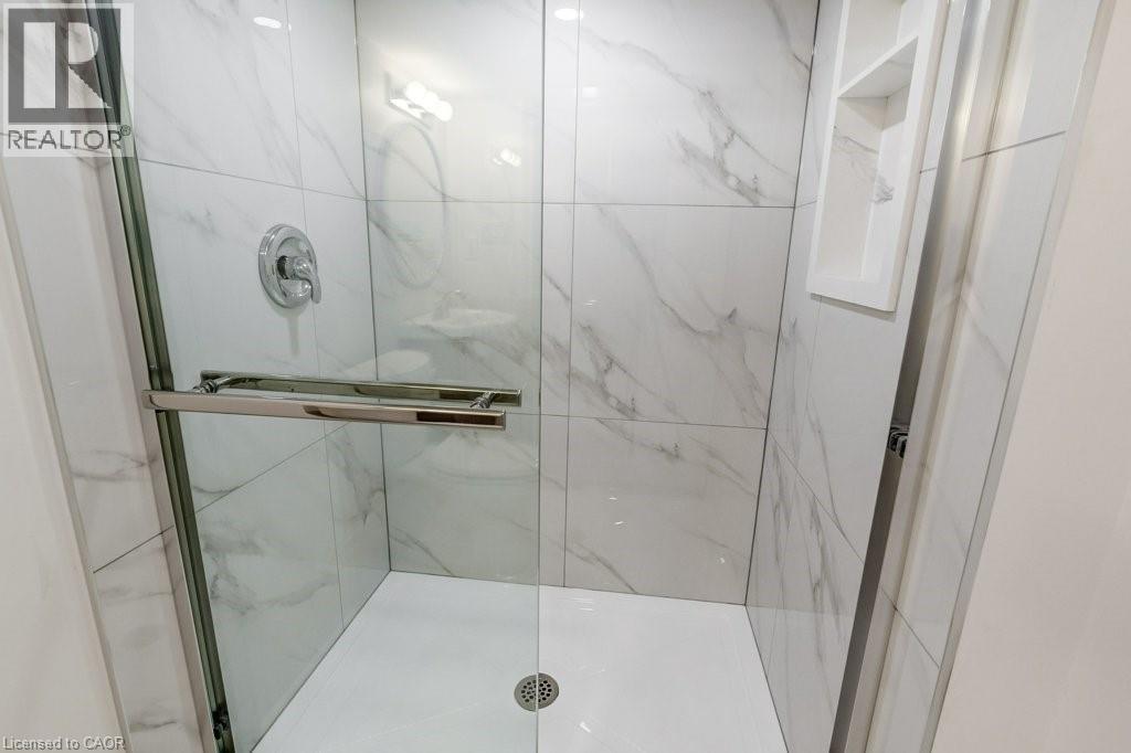 Walk-in shower featuring large format white tiled walls with subtle veining, clear glass enclosure with a chrome towel bar, chrome shower fixtures, and a built-in shower niche - 202 Erindale Avenue, Hamilton, ON