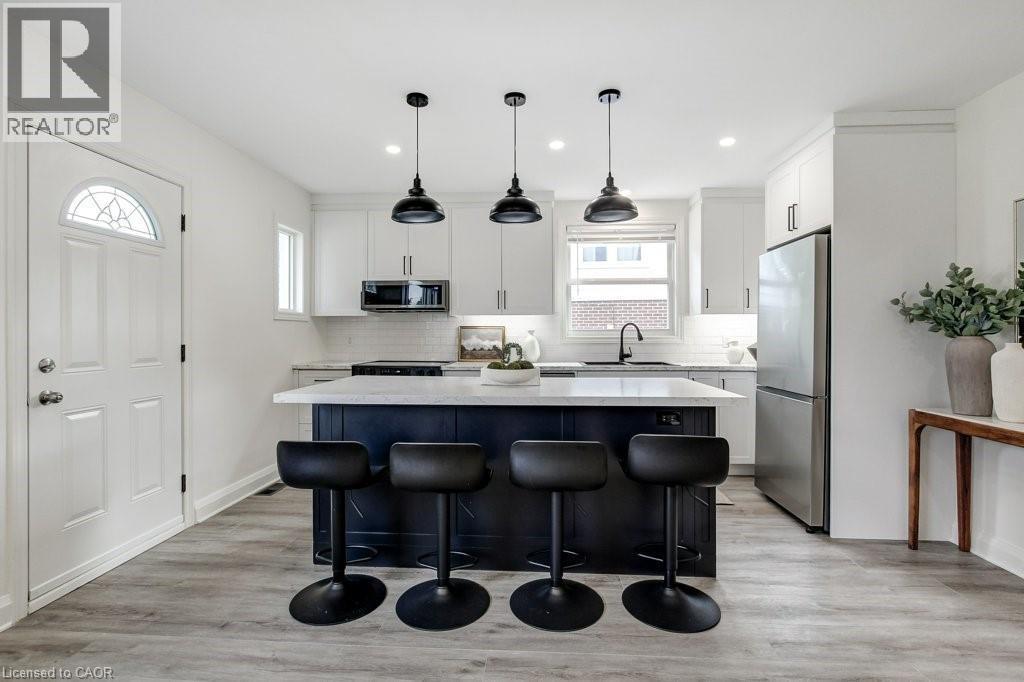 Modern kitchen featuring a large island with dark cabinetry and a light-toned countertop, complemented by three black pendant lights - 202 Erindale Avenue, Hamilton, ON
