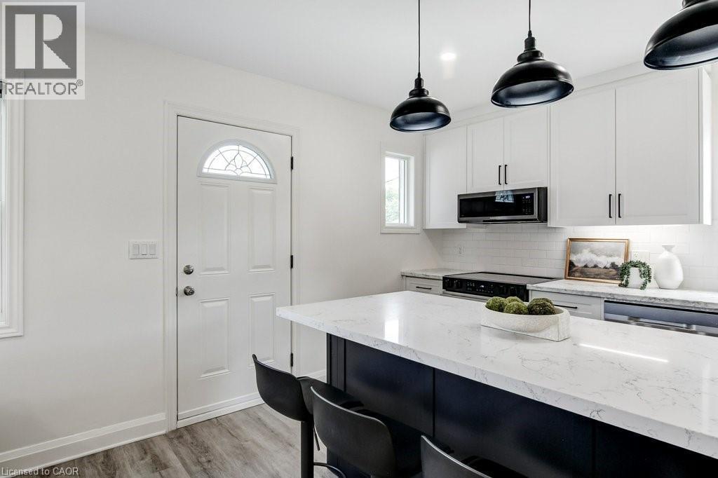 Kitchen featuring a substantial island with a light-toned countertop, white cabinetry, a subway tile backsplash, and wood-finish flooring - 202 Erindale Avenue, Hamilton, ON