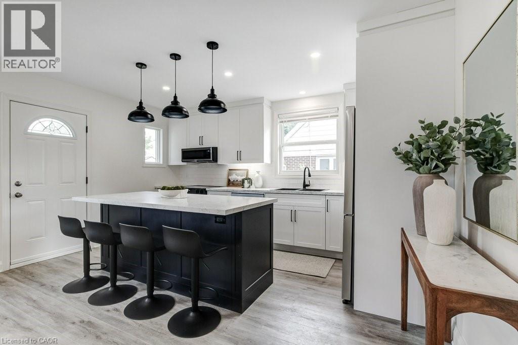 Kitchen featuring a dark-toned island with white countertop, three pendant lights, and light wood-finish flooring - 202 Erindale Avenue, Hamilton, ON