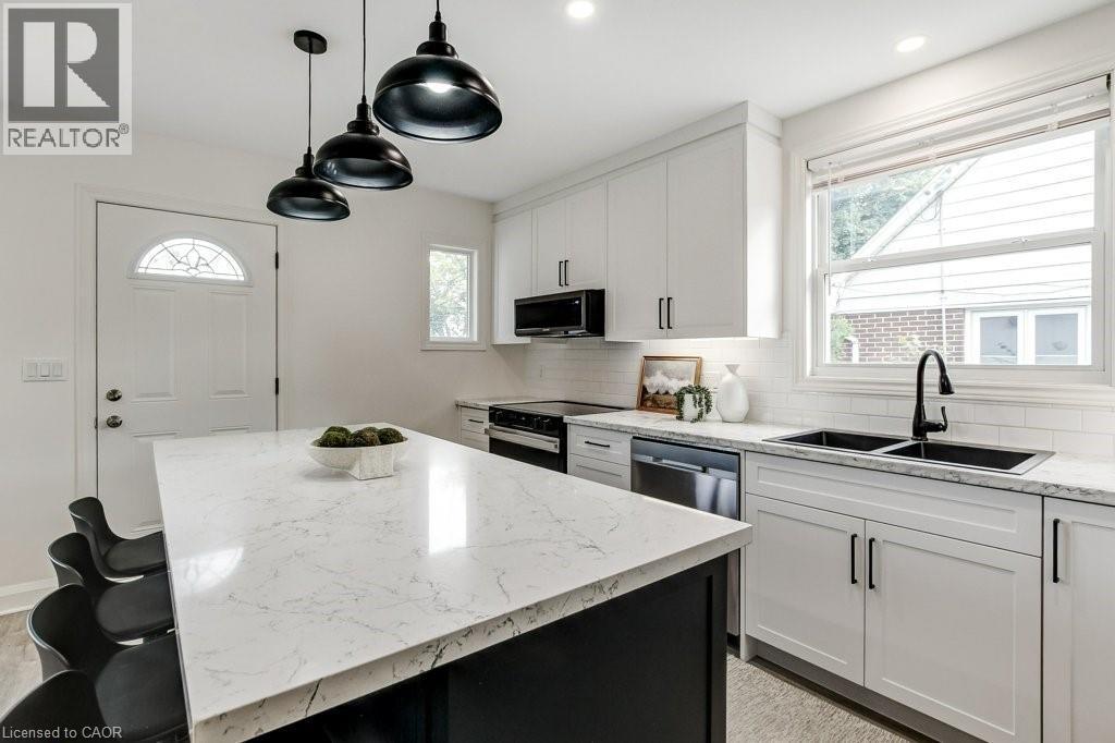 Kitchen featuring a large central island with a light-toned countertop, white cabinetry with matte black hardware, dual black basin sink with a matte black faucet, and stainless steel appliances - 202 Erindale Avenue, Hamilton, ON