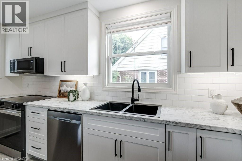 Kitchen featuring white shaker cabinetry, white subway tile backsplash, light-toned countertops, and a black double basin sink with a matte black faucet - 202 Erindale Avenue, Hamilton, ON