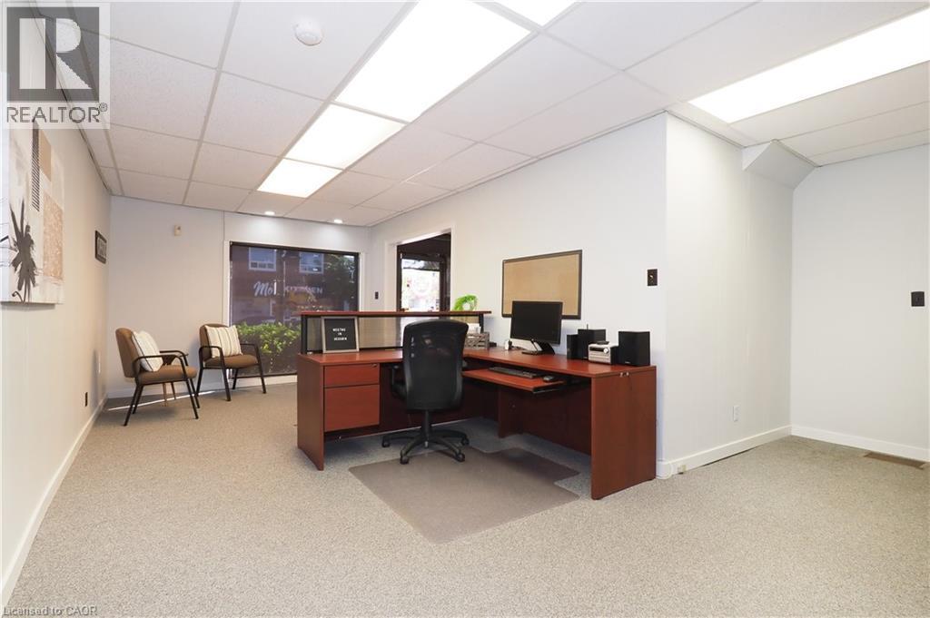 Carpeted interior space featuring a drop ceiling with integrated rectangular lighting panels, white walls, and a large front window - 731 King Street E, Cambridge, ON