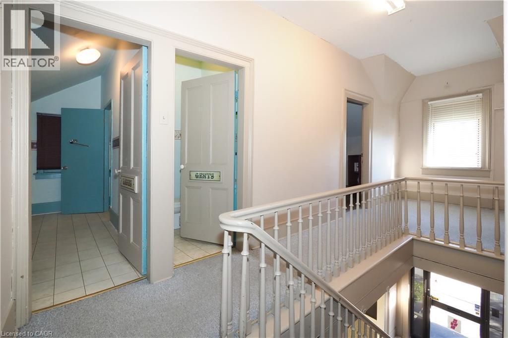 Upper level hallway with carpeted flooring, featuring multiple doorways, a window with blinds, and a staircase with a white spindle railing - 731 King Street E, Cambridge, ON