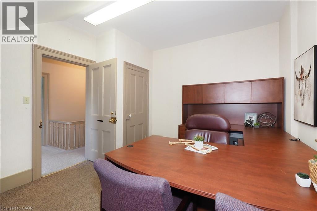 Office space featuring neutral wall paint, carpet flooring, a built-in wooden desk with upper cabinetry, and a flush-mounted ceiling light fixture - 731 King Street E, Cambridge, ON