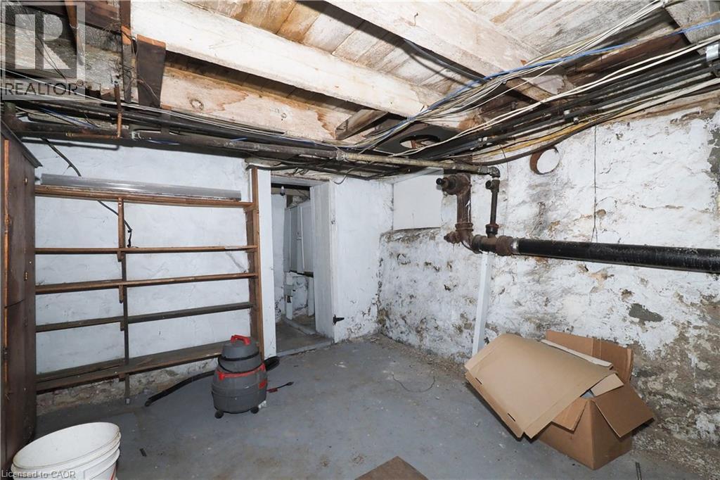 Exposed ceiling joists and utility lines featuring a concrete floor and painted stone foundation walls - 731 King Street E, Cambridge, ON