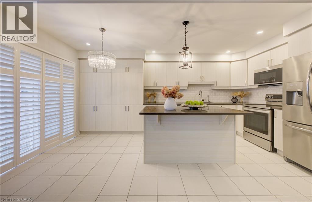 Kitchen featuring stainless steel appliances, a kitchen island, a breakfast bar area, light tile patterned floors, and backsplash - 302 Jean Landing, Milton, ON