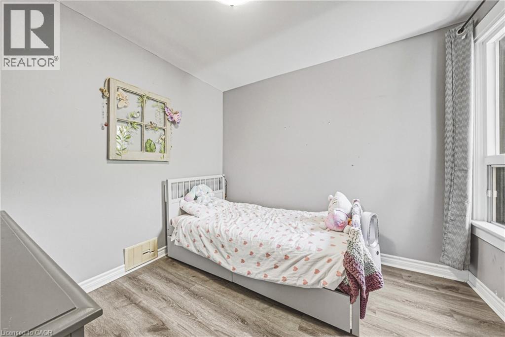 Neutral tone wall paint, wood-finish flooring, white baseboards, and a window with curtains - 47 Fraser Avenue, Hamilton, ON