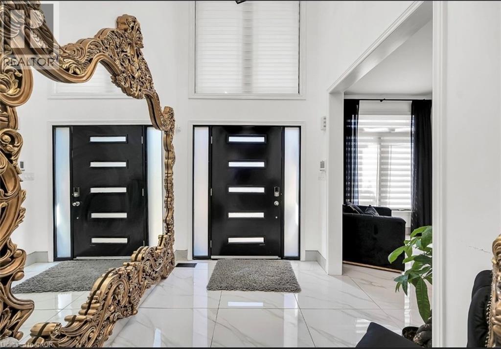 Spacious entryway featuring polished white tile flooring, two modern black doors with integrated horizontal window panels, and a prominent ornate gold-toned mirror - 137 Diiorio Circle, Ancaster, ON
