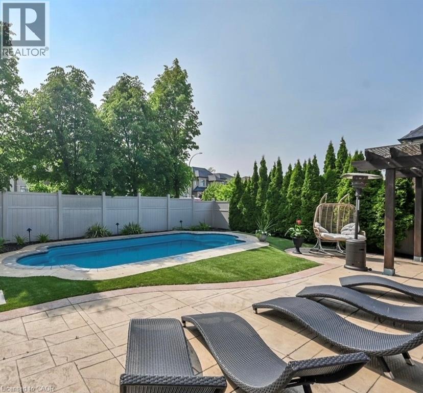 Resort-style backyard featuring a kidney-shaped swimming pool, stamped concrete patio, and a wooden pergola structure - 137 Diiorio Circle, Ancaster, ON