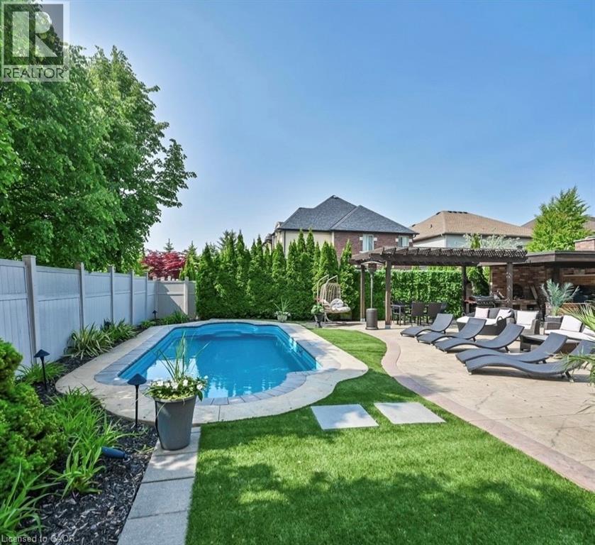 Rectangular swimming pool with stone coping, surrounded by artificial turf and mature landscaping - 137 Diiorio Circle, Ancaster, ON