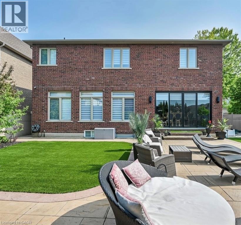 Rear elevation featuring brick exterior, a patio with stone paver flooring, synthetic lawn, and large sliding glass doors - 137 Diiorio Circle, Ancaster, ON