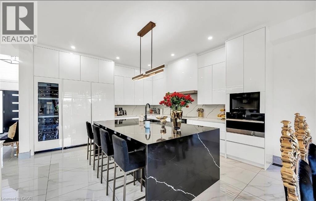Modern kitchen featuring a large waterfall island with a dark stone countertop, integrated wine cooler, built-in oven, and recessed lighting - 137 Diiorio Circle, Ancaster, ON