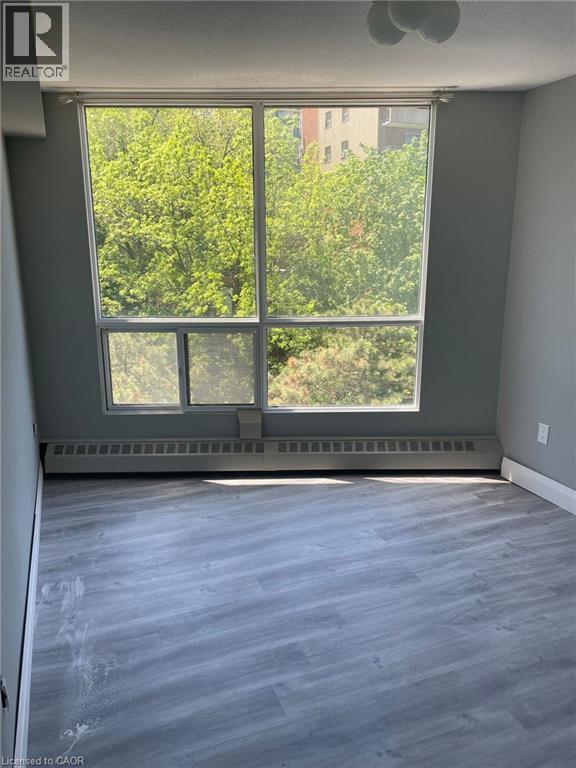 Expansive window offering a green exterior backdrop, complemented by light gray walls and wood-finish flooring - 150 Charlton Avenue E Unit# 708, Hamilton, ON