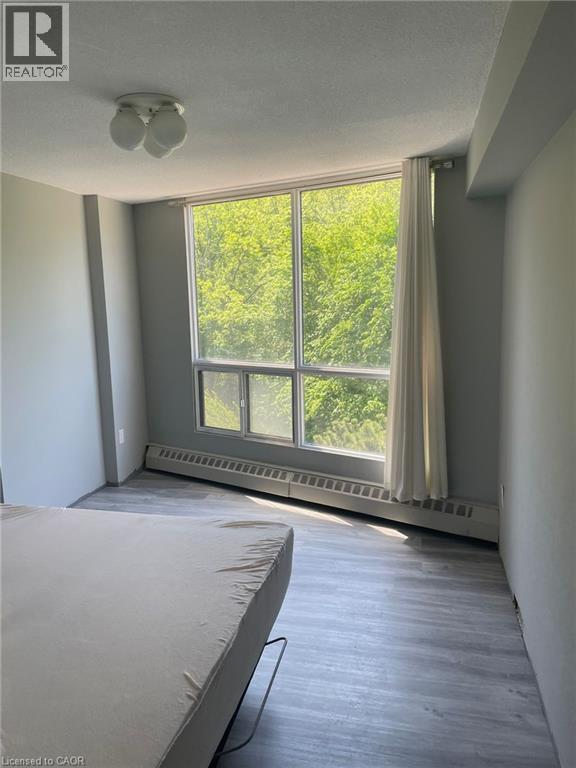 Room featuring a large window, light wood-finish flooring, and a ceiling-mounted light fixture - 150 Charlton Avenue E Unit# 708, Hamilton, ON