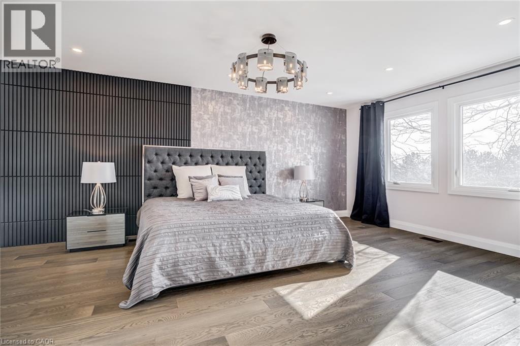 Wood-finish flooring throughout, featuring a tufted headboard, recessed ceiling lighting, a contemporary chandelier, and a decorative accent wall - 1320 Monmouth Drive, Burlington, ON