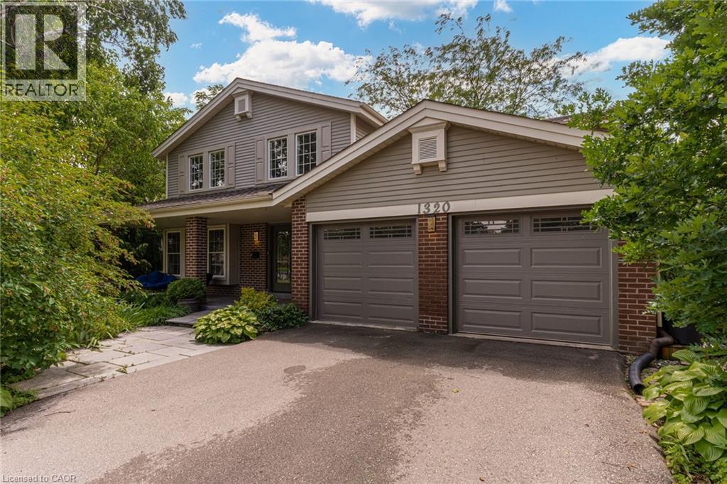 Exterior featuring gray siding, brick accents, and two garage doors with transom-style windows - 1320 Monmouth Drive, Burlington, ON