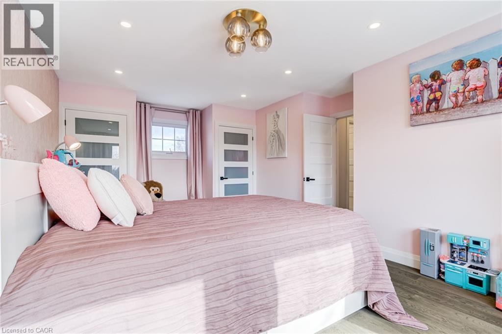 Bedroom featuring recessed lighting, a modern ceiling fixture, wood-finish flooring, and white interior doors with opaque glass panels - 1320 Monmouth Drive, Burlington, ON