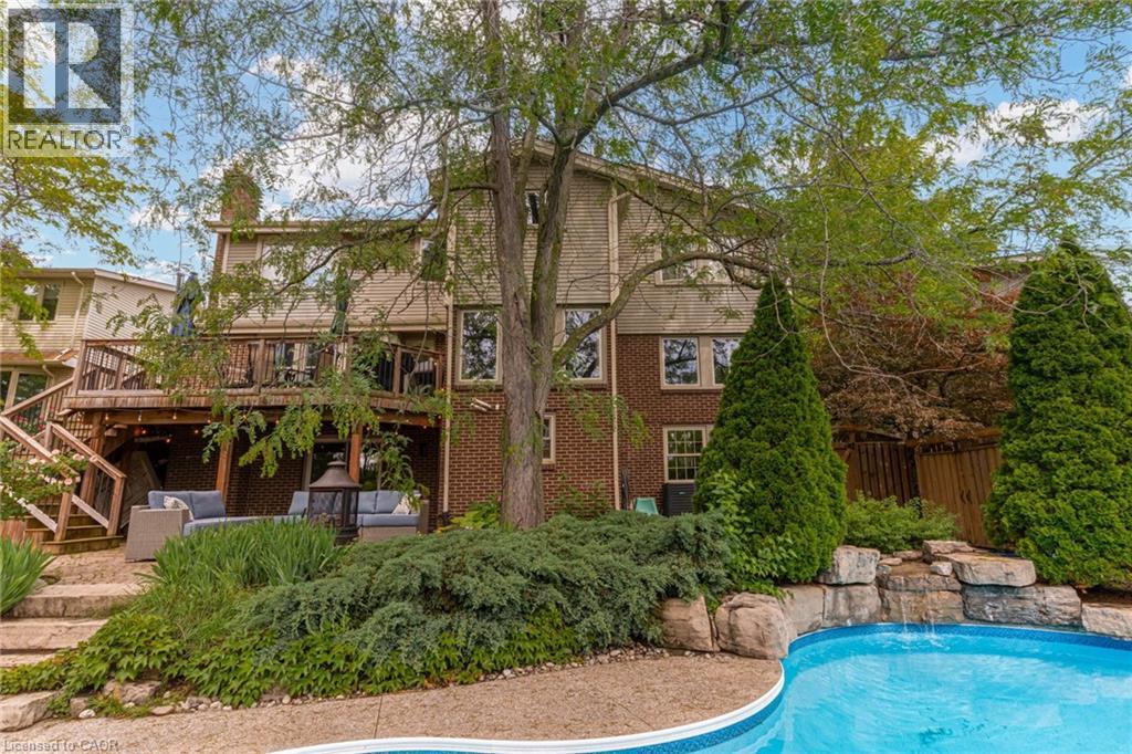 Rear exterior featuring a multi-level deck, a lower patio, and an in-ground pool with a rock waterfall - 1320 Monmouth Drive, Burlington, ON