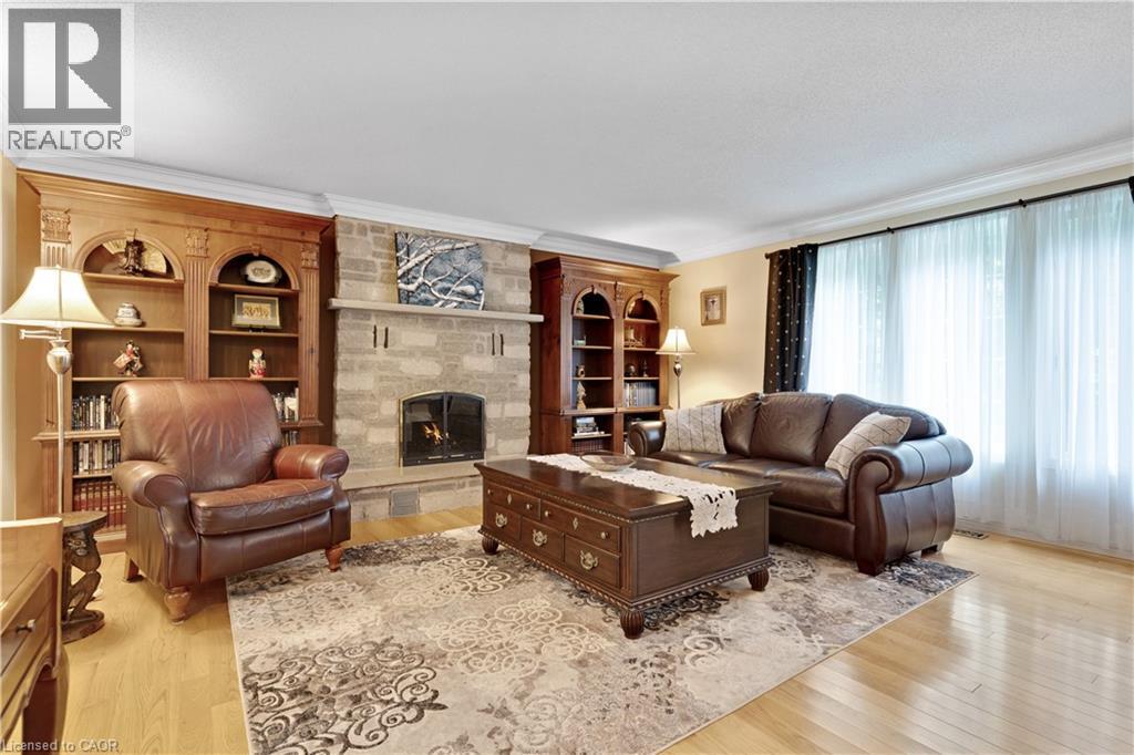 Living room featuring a stone fireplace with hearth, wood-finish flooring, and crown molding - 110 Grand Ridge Drive, Cambridge, ON