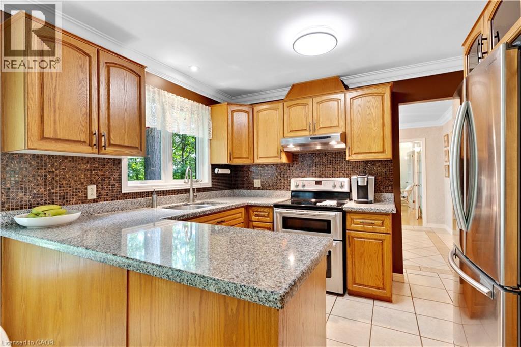 U-shaped kitchen featuring wood cabinetry, speckled countertops, a brown mosaic tile backsplash, a stainless steel electric range, and tile flooring - 110 Grand Ridge Drive, Cambridge, ON