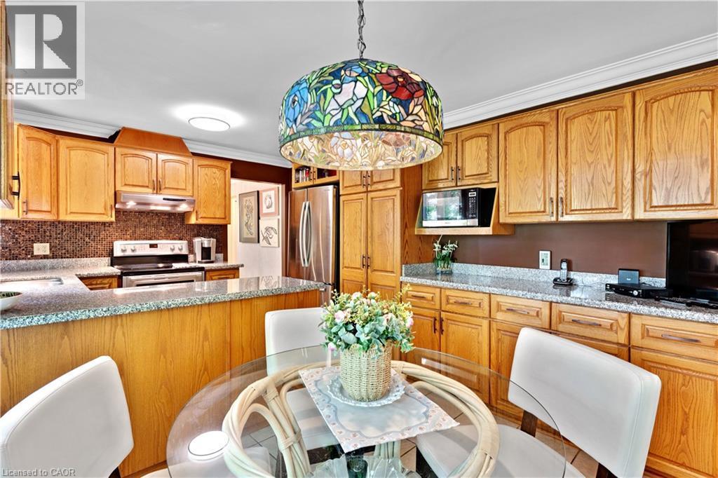 Kitchen featuring a stained glass pendant light, wood cabinetry, granite-finish countertops, tile backsplash, and stainless steel appliances - 110 Grand Ridge Drive, Cambridge, ON
