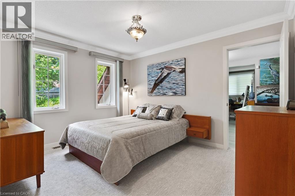Carpeted bedroom featuring two large windows with exterior views of mature trees, a built-in wall-mounted side table, and recessed lighting - 110 Grand Ridge Drive, Cambridge, ON