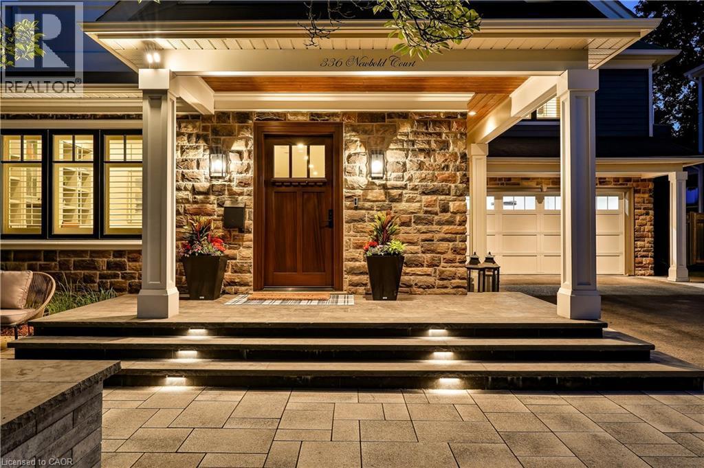 Stone facade entry with a wood front door, covered porch, integrated step lighting, and an attached two-car garage - 336 Newbold Court, Burlington, ON
