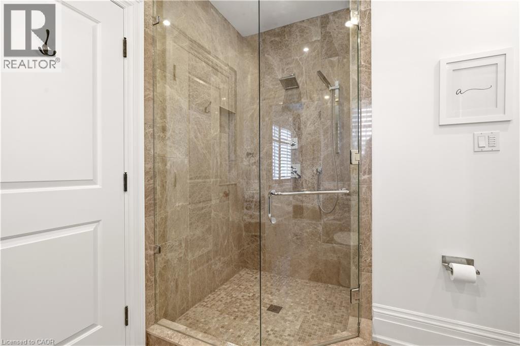 Glass-enclosed shower featuring full-height stone tile walls, a rain showerhead, a handheld shower fixture, and a pebble-style floor - 336 Newbold Court, Burlington, ON